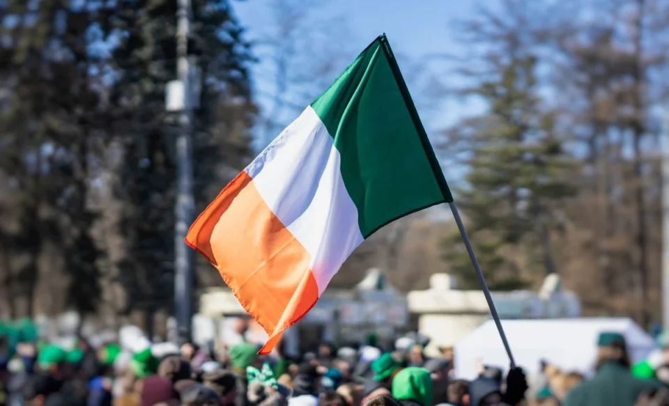 NA IMAGEM MOSTRA A BANDEIRA DA IRLANDA E PESSOAS ATRÁS NAS RUAS DA CAPITAL